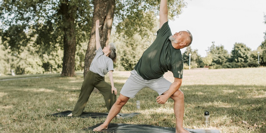 Picture of a man and women performing yoga under the shed of a tree