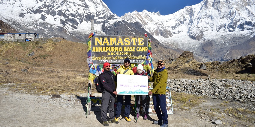 Four trekkers at Annapurna Base Camp with a Heaven Himalaya banner, showcasing treks.