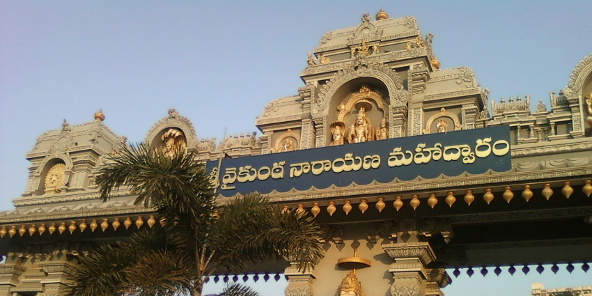 A picture of a road's entry gate with a sculpture of Lord Ganesh on the walls surrounded by greenery