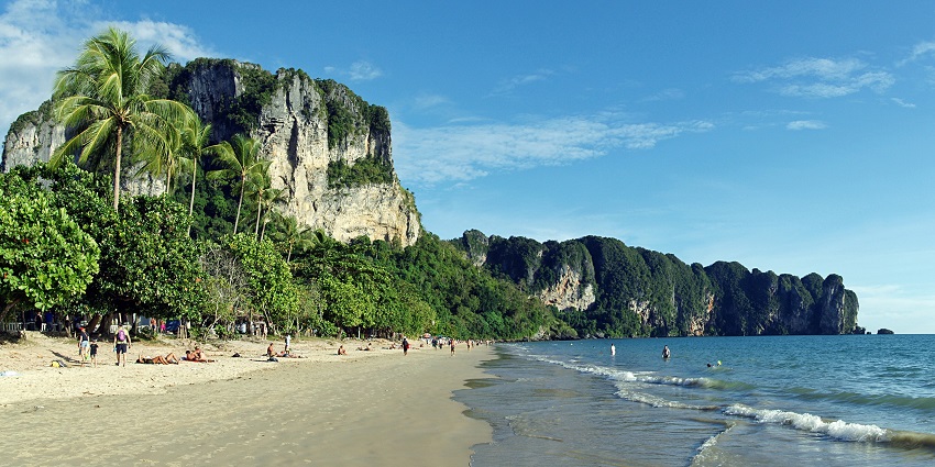 View of Ao Nang beach surrounded by lush green mountains and clear water under clear sky.