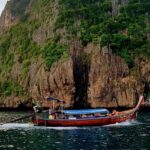 An image of a red boat on a body of water near a brown cliff during daytime in Ao Nang.