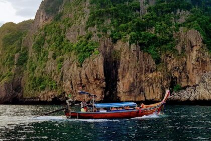 An image of a red boat on a body of water near a brown cliff during daytime in Ao Nang.