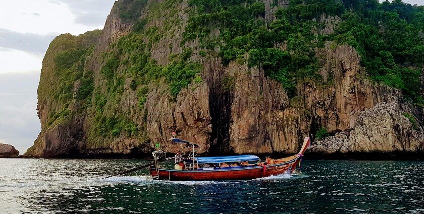 An image of a red boat on a body of water near a brown cliff during daytime in Ao Nang.