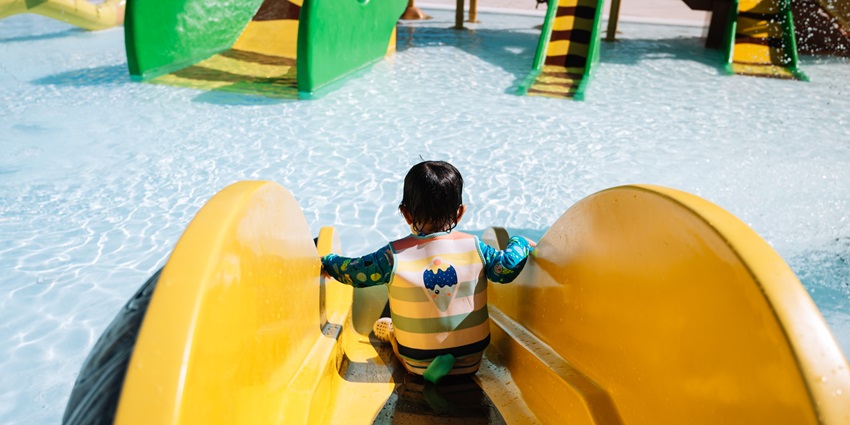 Image of a boy in yellow swim suit enjoying the water slides and other rides
