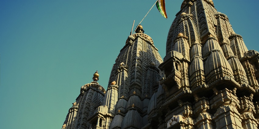 Intricately carved spires of a traditional Indian temple rise against a serene teal sky.