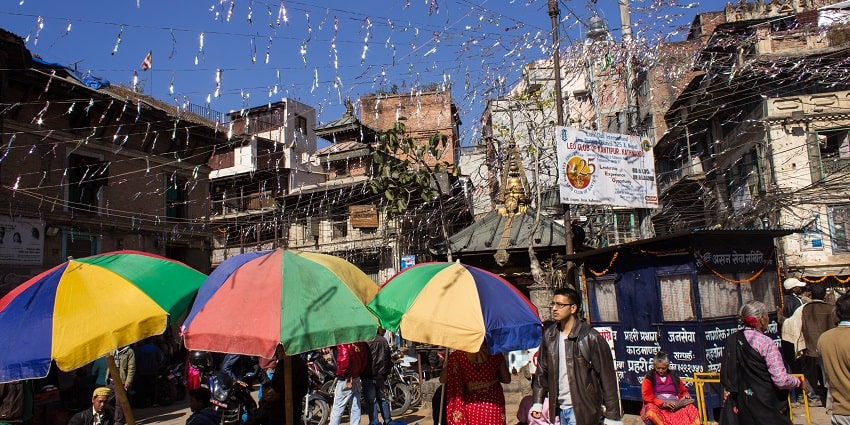 A bustling Asan Bazaar filled with vibrant stalls, shoppers, and colourful goods all around.