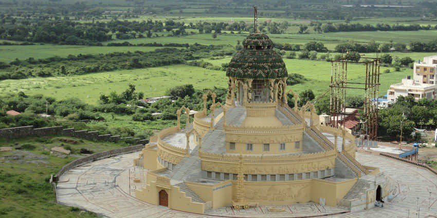 Aerial view of the Jain temple surrounded by lush gardens , shrubs and trees