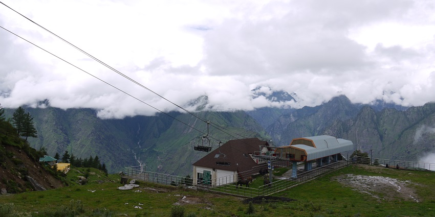 A scenic view of Auli Ski Resort in summer, showcasing lush green hills and clear skies.