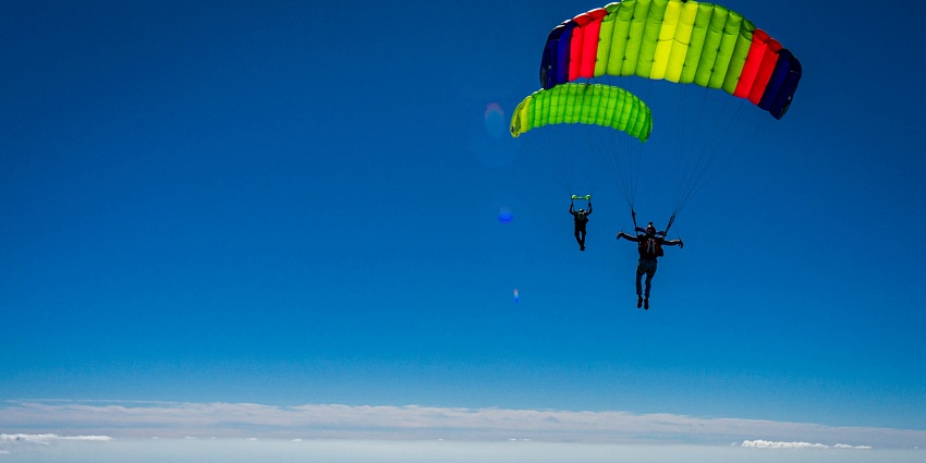 An image of a two skydivers falling down the clear blue sky with parachutes