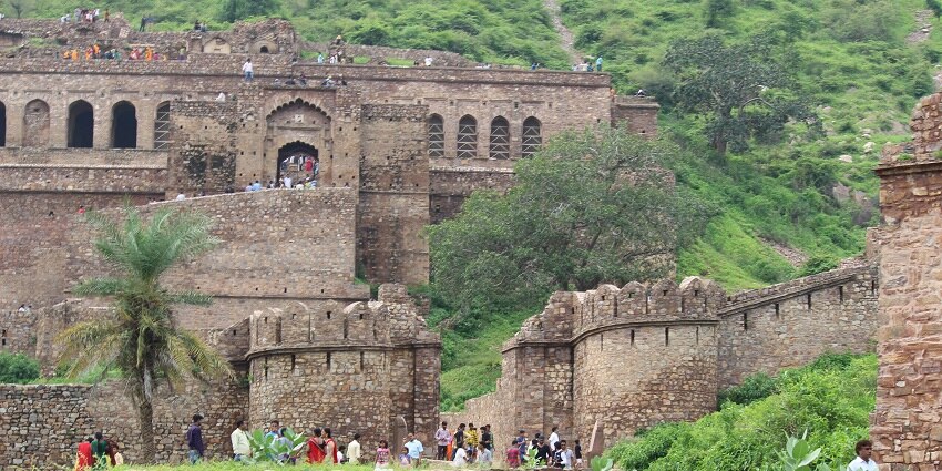 The view of Bhangarh Fort with several tourists and the Royal Palace ruins behind.