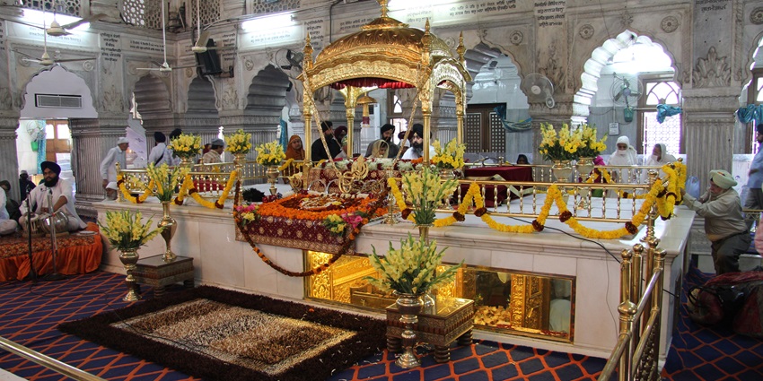 A picture of the interiors of a gurudwara with devotees worshipping the main prayer sanctum