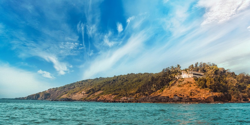 Image of Baga beach with clear blue water surrounded by greenery and a market nearby.