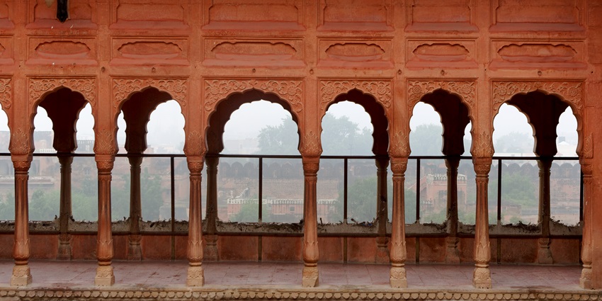 A picture of a historical monument with tall, red outer walls and a surrounding garden