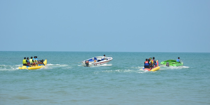 A banana boat filled with people being pulled across the sea by a motorboat.
