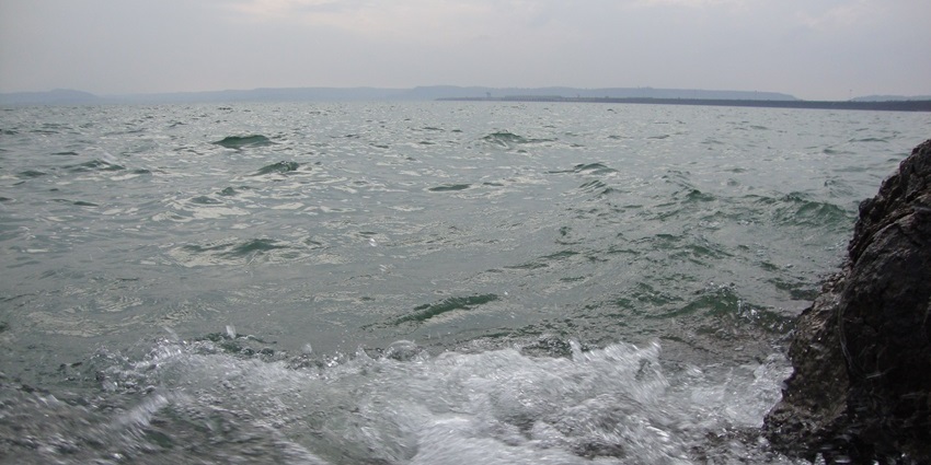 Bargi Dam reservoir with calm waters, tree-covered shoreline, and hazy sky backdrop