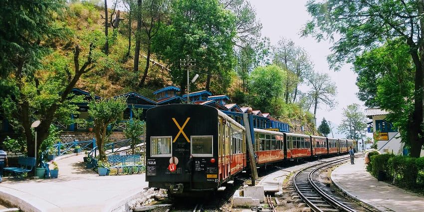 mage of black and red train on the track surrounded by lush green mountains in Barog