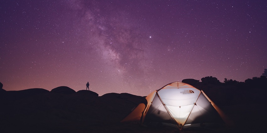 Camping in Solan on a hillside with a man’s silhouette standing nearby, gazing at the sunset.