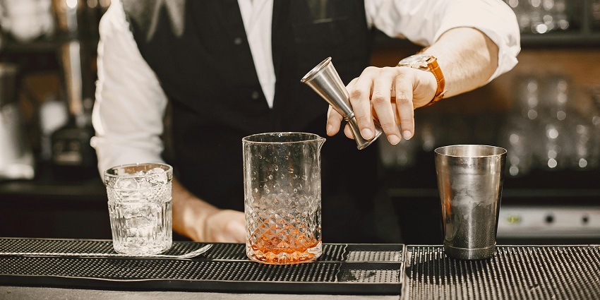 Image of bartender skillfully mixes a colourful cocktail at a lively bar, showcasing their craft.