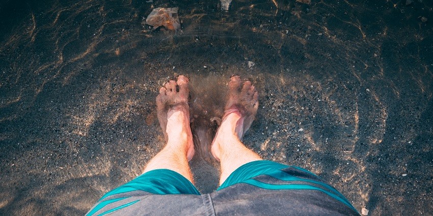 Person’s bare feet partially dipped in water creating soft ripples in Deulajhari Hot Spring.