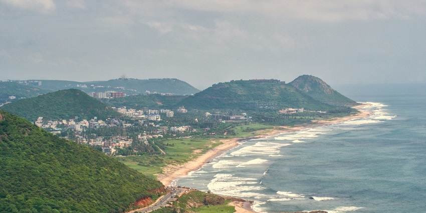 A breathtaking view of a beach in Visakhapatnam surrounded by lush greenery in the day.