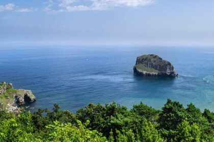 A beach featuring rugged sea cliffs, a rocky shore, and a distant church on the horizon.