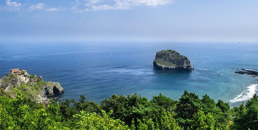 A beach featuring rugged sea cliffs, a rocky shore, and a distant church on the horizon.