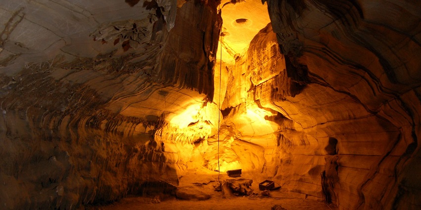 Illuminated Belum cave with rugged rock formations, glowing in golden light from within