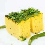 A mouth-watering view of a plate served with yellow dhokla garnished with coriander.