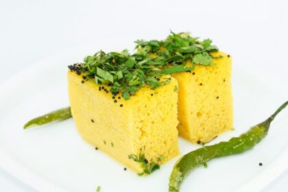 A mouth-watering view of a plate served with yellow dhokla garnished with coriander.