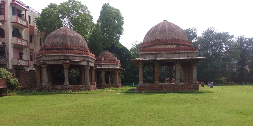 A picture of the Hauz Khas fort in Delhi with a big garden in front of it and trees in the background