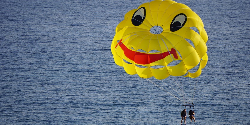 A person parasailing in Pattaya in a yellow parachute with mountains in the background.