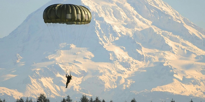 Man flying on a parachute near lush trees, experiencing the thrill of skydiving in Pokhara.