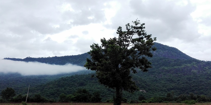 A picture of a green mountain near Dharmatma Waterfalls under a huge cloud