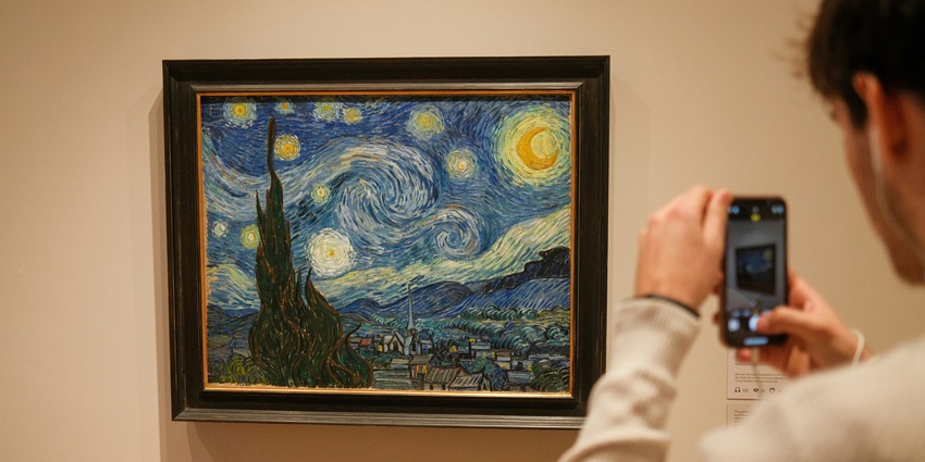 Image of a man taking pictures of iconic starry night Van Gogh painting in a museum