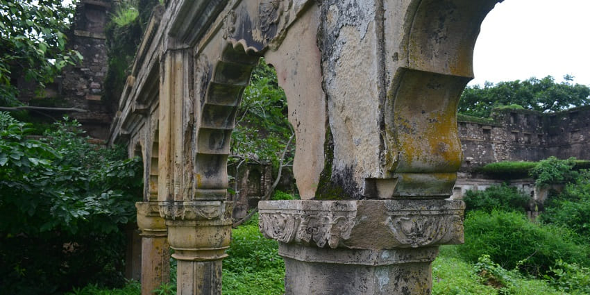 Pillars of a ruined building and fort surrounded by lush greenery during day time