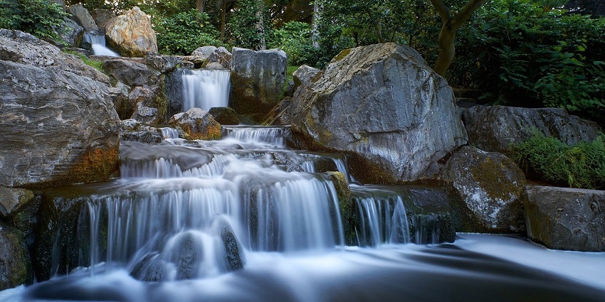 Waterfall cascades through a lush green forest, surrounded by vibrant foliage and natural beauty