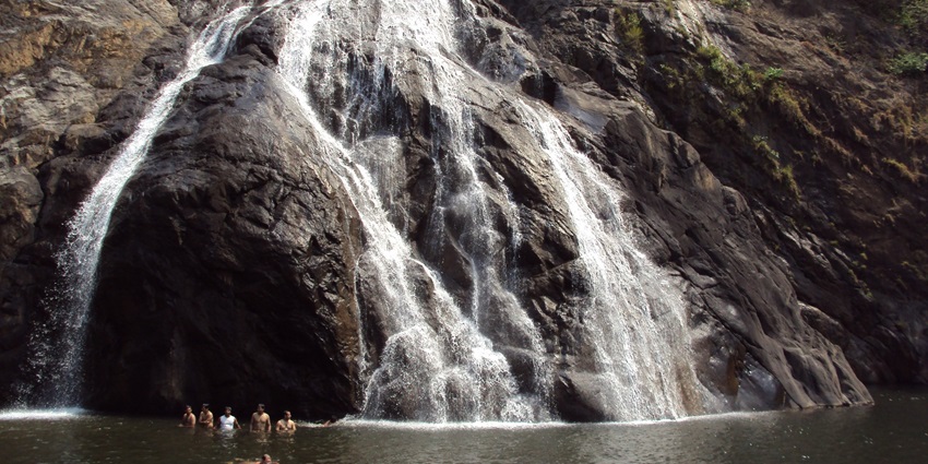 A mesmerising view of a waterfall in Goa surrounded by lush greenery during the day.