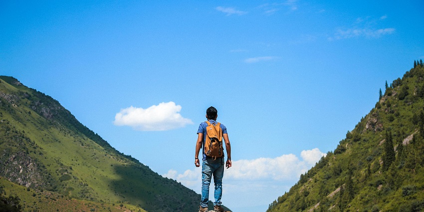 Image of a man standing on a rock mountains, surrounded by lush greenery hills