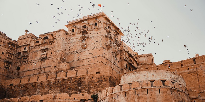A picture of a fort in India with birds flying over it during daytime