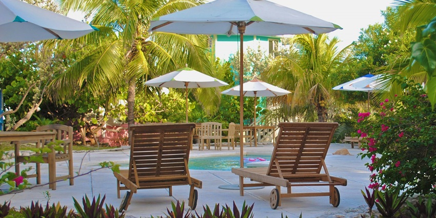 Two brown wooden lounge chairs by a pool, set against a sunny, relaxing backdrop in a resort.