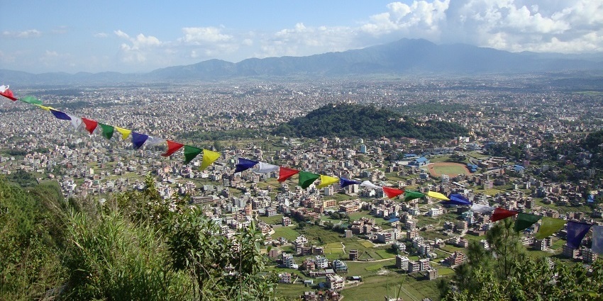 Panoramic view of Kathmandu Valley, showing a sprawling city with buildings and hills.