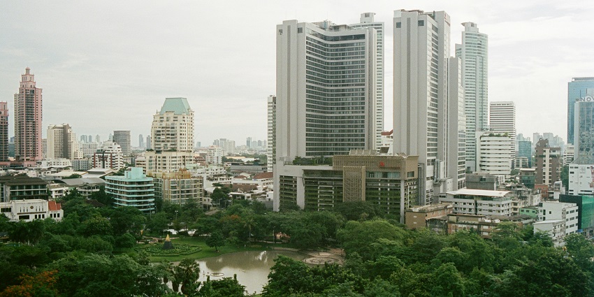 A mesmerising view of Bangkok with high rise buildings, lush greenery and a water body.