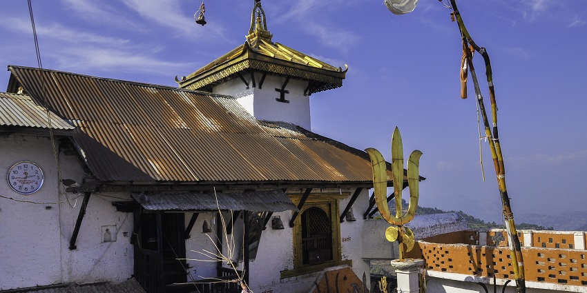 Bhairabsthan Temple in Palpa with a white wall, golden roof, and a trident flag.