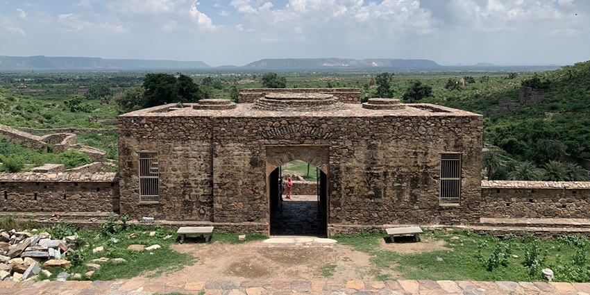 The ruins of Bhangarh Fort's Royal Palace in Rajasthan, are surrounded by greenery and an overcast sky.