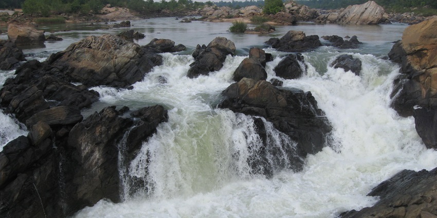 Bhimkund falls is surrounded by rocky terrain and lush greenery.
