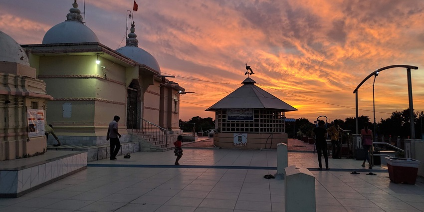 The sun sets behind Bhimnath Mahadev Temple in Gujarat, creating a picturesque scene.