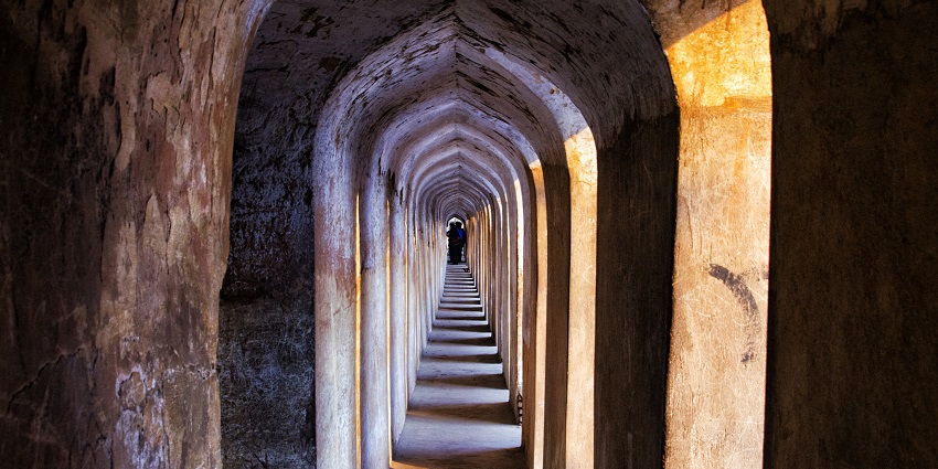 A narrow, arched corridor with golden and blue hues, showcasing intricate Bhool Bhulaiya