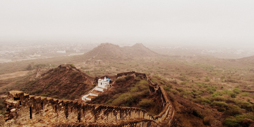 An aerial picture of a long wall built on a mountain, leading to a fort