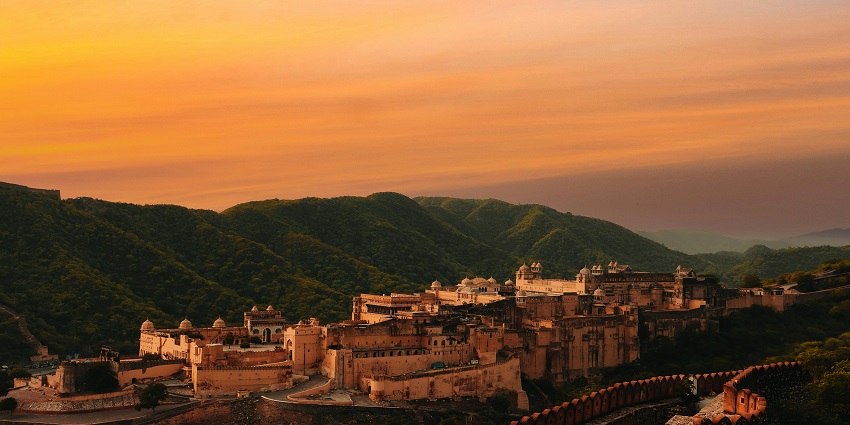 Picturesque view of village and fort surrounded by lush green hills during sunset time