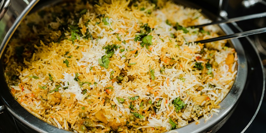 A pan on a stove filled with biryani and topped with vibrant green vegetables.
